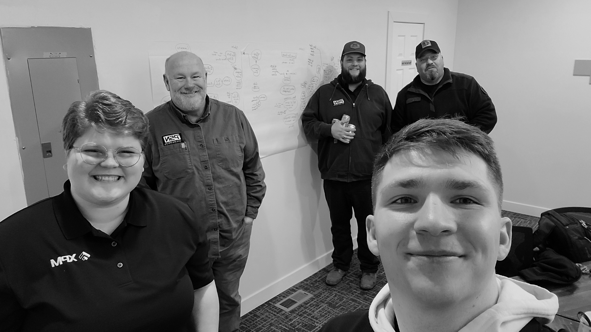 Group of five people smiling, posing near a whiteboard, indoor setting, black and white photo.