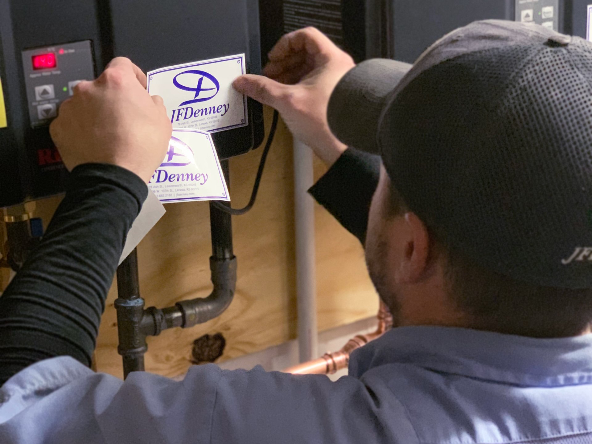 A man wearing a hat is putting a sticker on a pipe