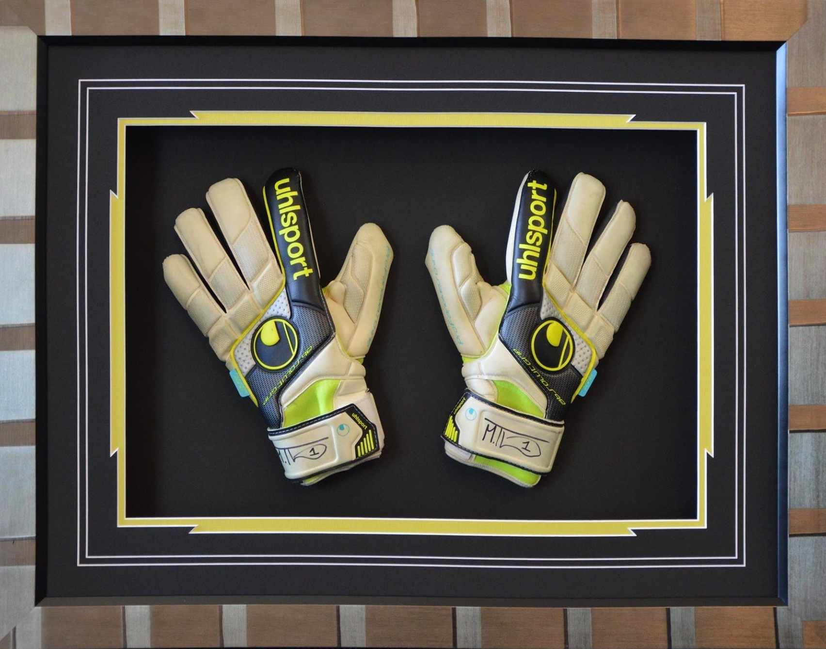 Framed display of black-and-yellow goalkeeper gloves mounted on a wall