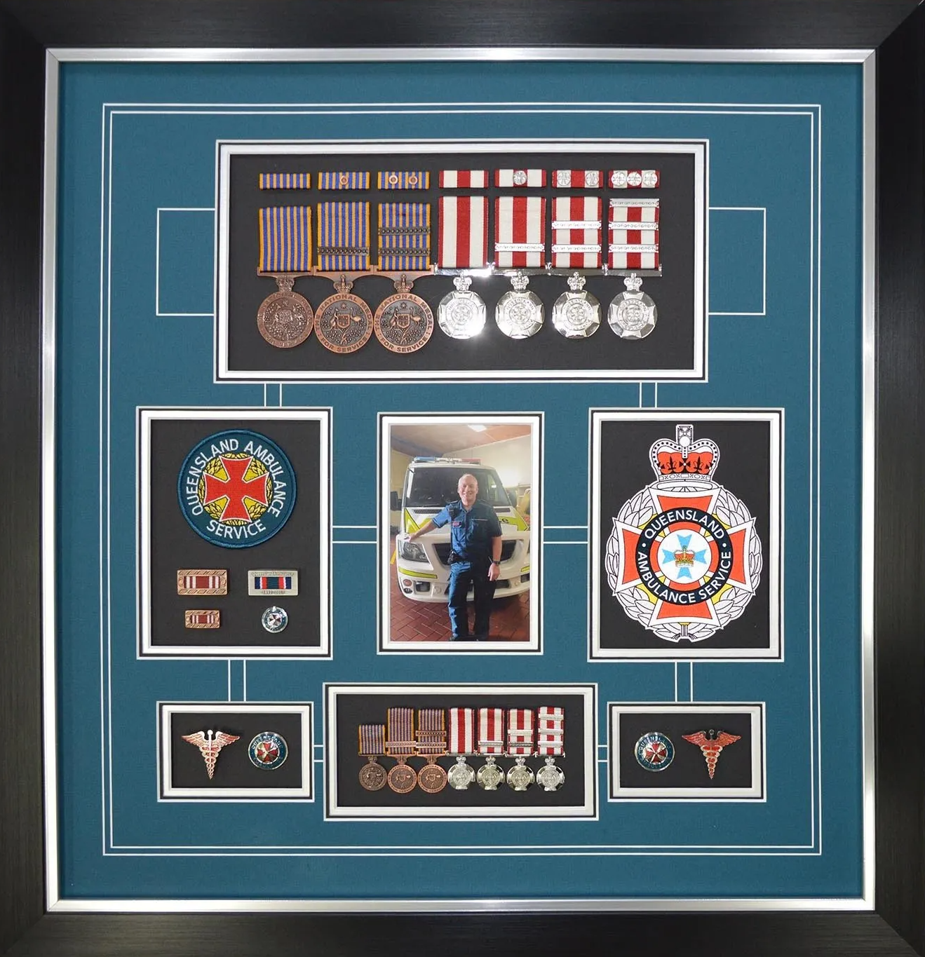 Framed display of military medals, badges, and patches on a teal background