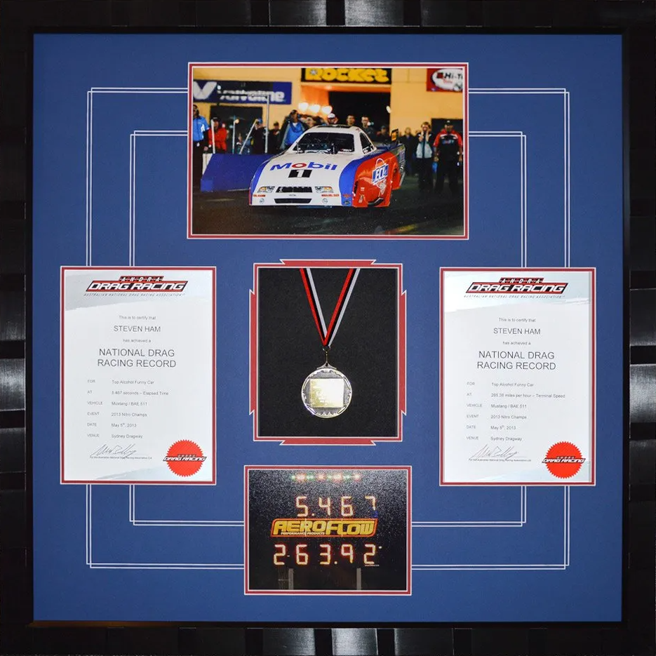 Framed racing memorabilia display with a photo, medal, certificates, and a plaque on a blue background