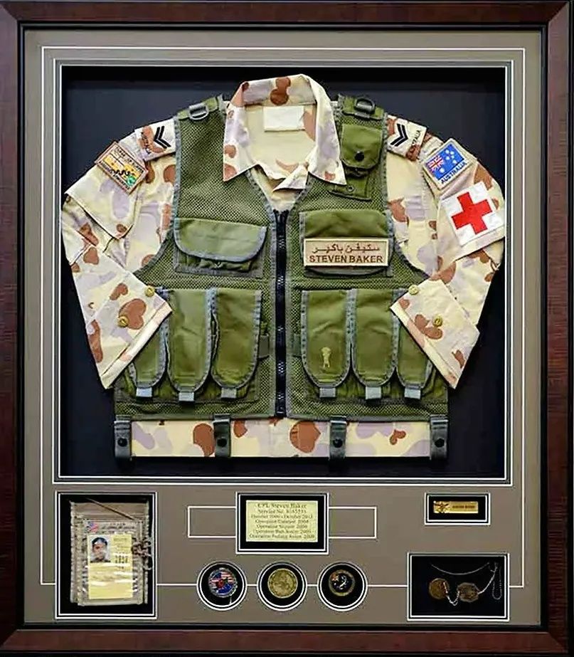 Framed military vest and camouflage uniform display with patches, medals, and a Red Cross armband