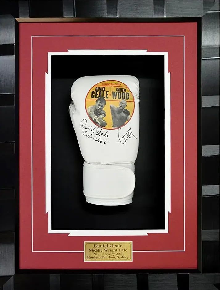 Framed white boxing glove display with red mat and gold plaque in a glass case