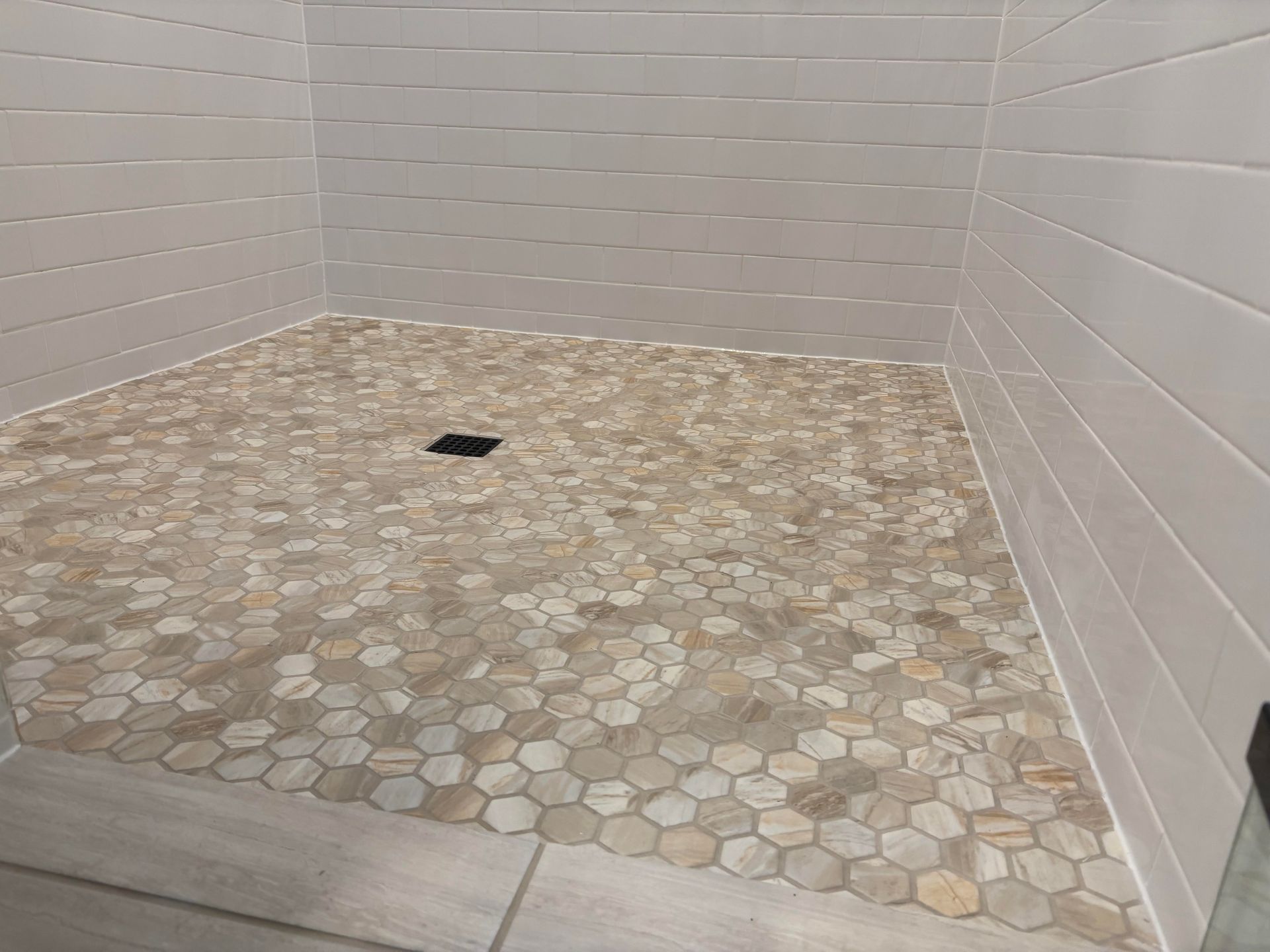 A tiled shower stall featuring a stone-look bench, a mosaic accent strip, and a recessed black-shelved wall niche.