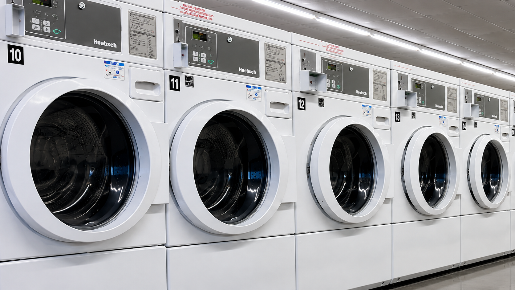 Row of white front-loading washing machines in a laundromat, viewed from the front