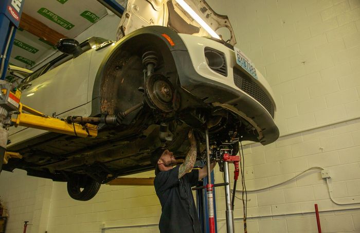 Mechanic working under a white car lifted on a hydraulic garage hoist | Bay's Auto Repair & Collision Services