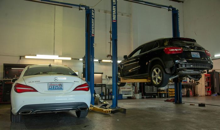 Two cars in an auto shop lift bay, one white sedan and one black SUV raised on a hydraulic lift. | Bay's Auto Repair & Collision Services