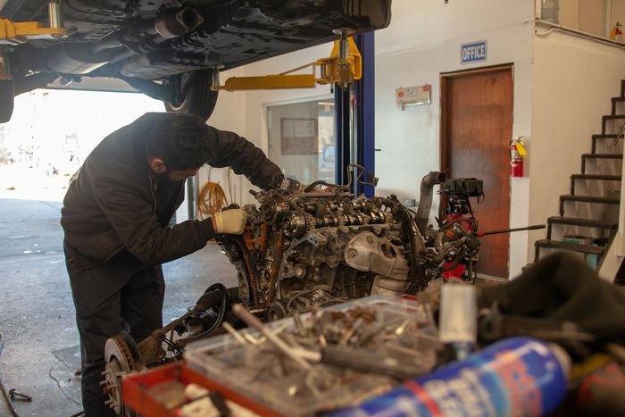 Mechanic working on a car engine in a garage, with a lifted vehicle overhead and tools in the foreground | Bay's Auto Repair & Collision Services