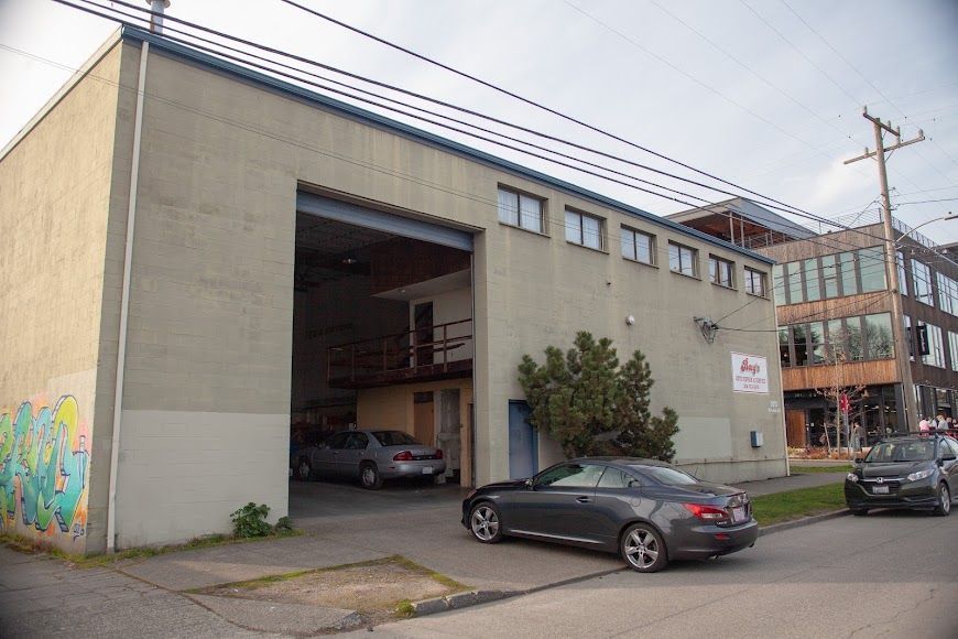 Industrial warehouse with open garage bay and parked cars on a street corner | Bay's Auto Repair & Collision Services