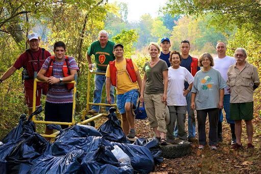 Group of volunteers standing beside bags of collected trash in a wooded park area