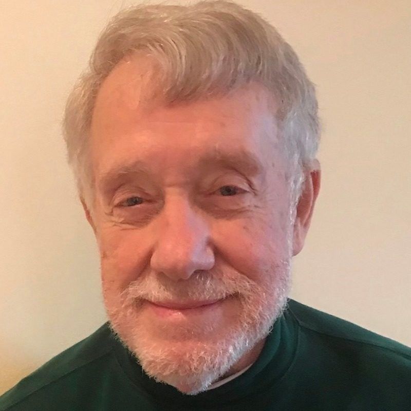 Close-up portrait of a smiling man with gray hair and beard against a plain light background