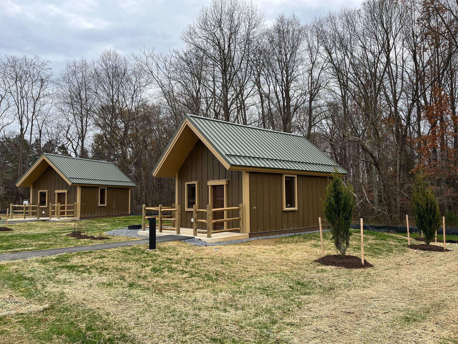Two small wooden cabins in a grassy clearing with leafless trees in the background
