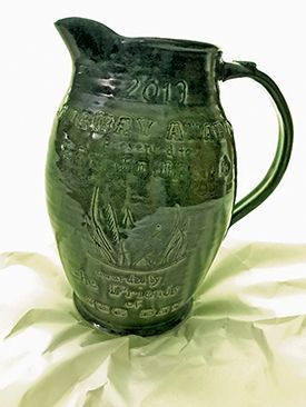 Green decorative pitcher with handle and raised design on a light cloth background