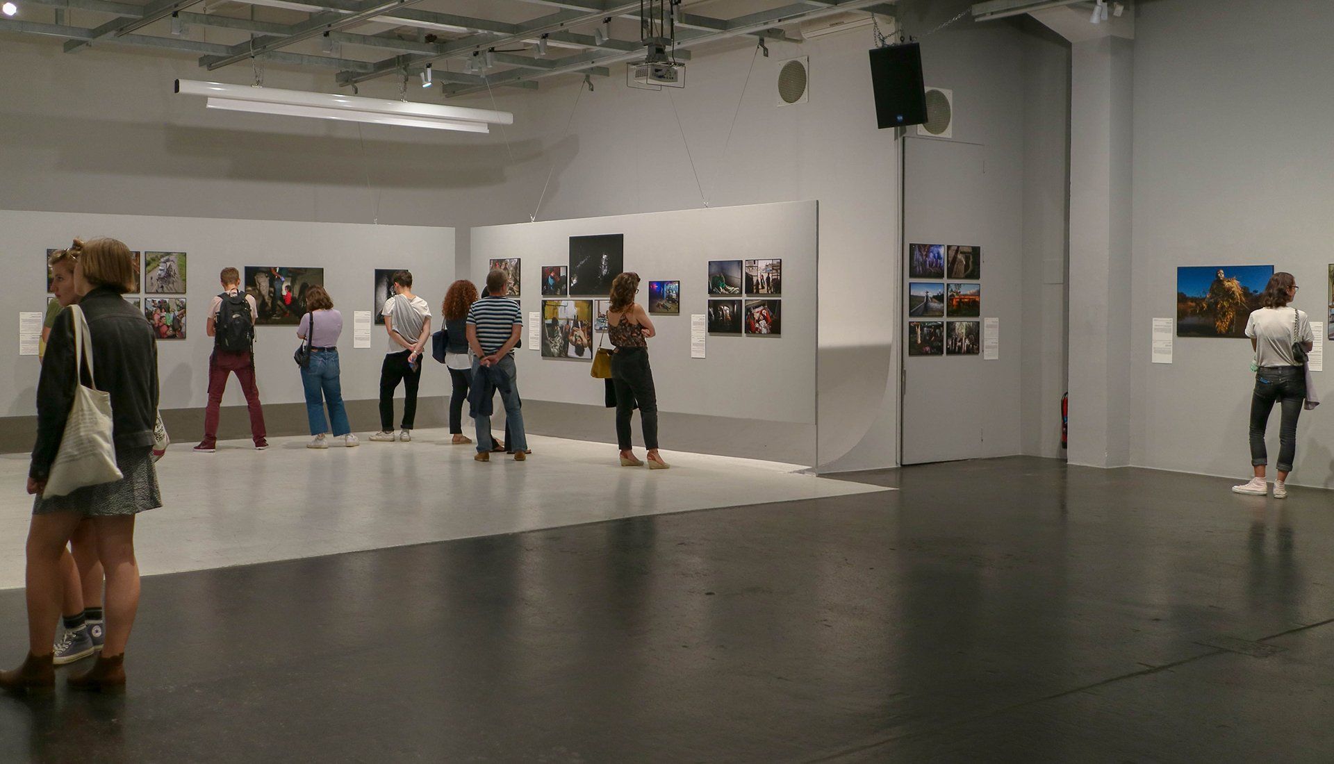 People viewing artwork in a white-walled gallery with a mirrored display and framed pieces.