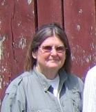 Woman in sunglasses and gray jacket standing in front of a red wooden wall
