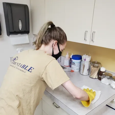 Person wiping a countertop in a break room with a yellow cloth