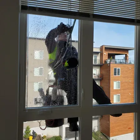 Person cleaning an outside window, seen through a rainy pane, with apartment buildings in the background