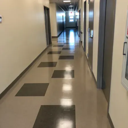 Empty hallway with beige walls and dark floor tiles leading to a bright doorway.