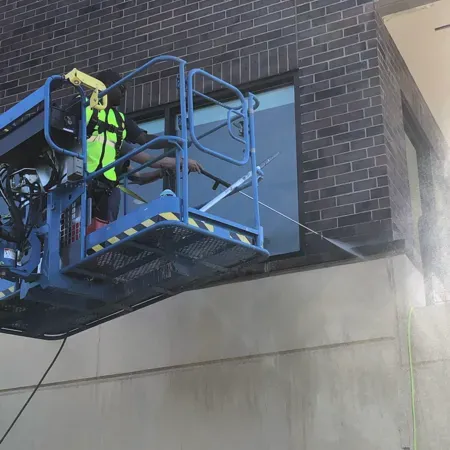 Worker in neon safety gear on a blue lift repairing a brick building exterior