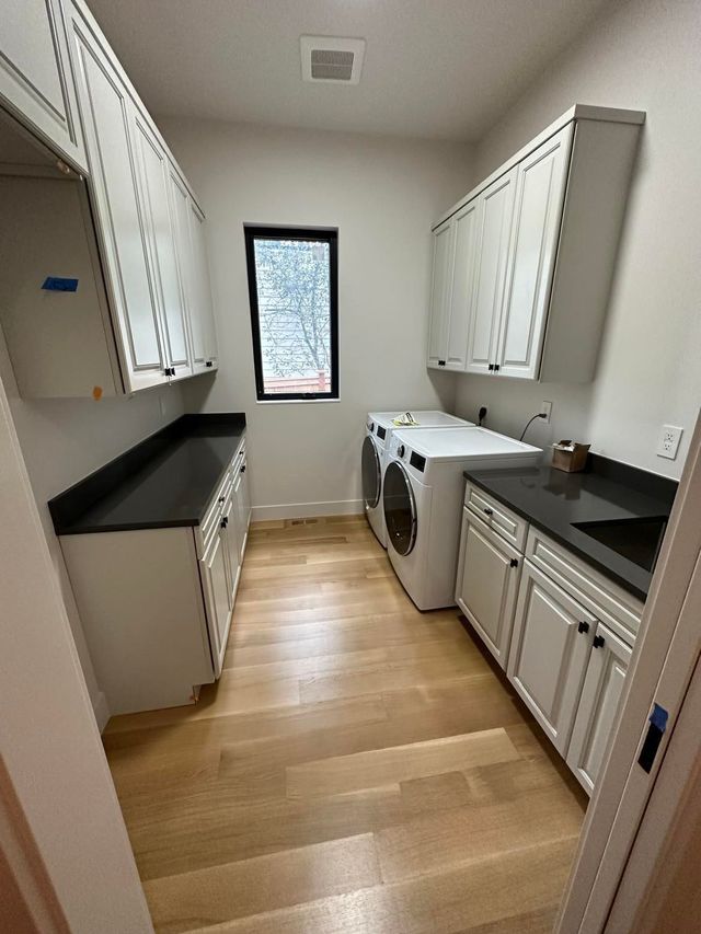 Narrow galley kitchen with white cabinets, black countertops, and a small window at the far end.