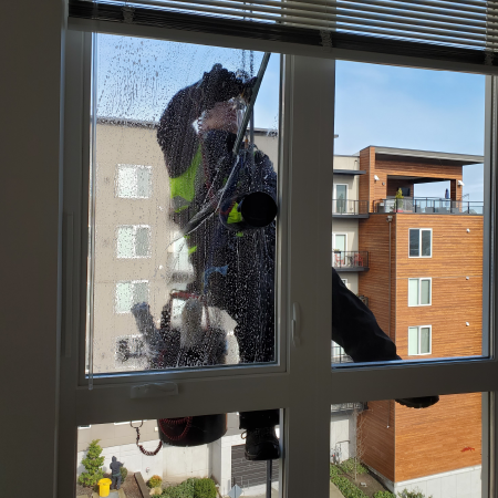 Window cleaner on exterior of high-rise window, seen through wet glass, with apartment buildings outside