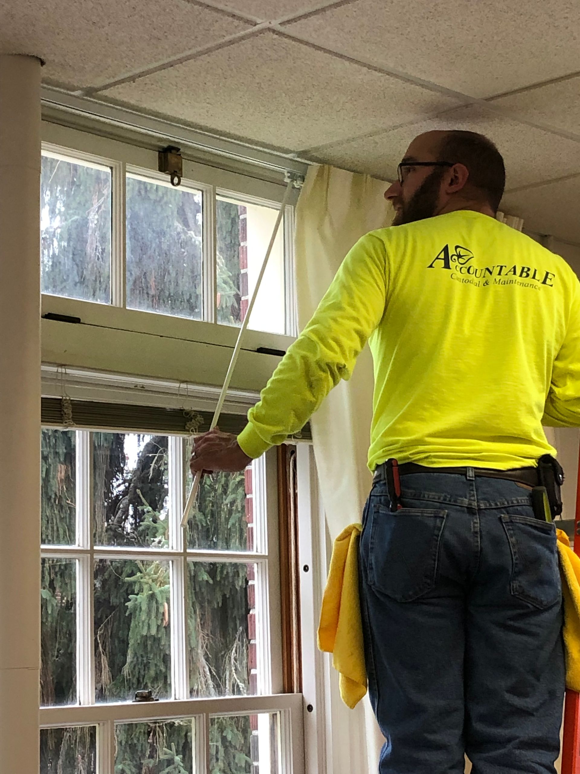 Worker in neon yellow shirt cleaning a window with a cloth indoors