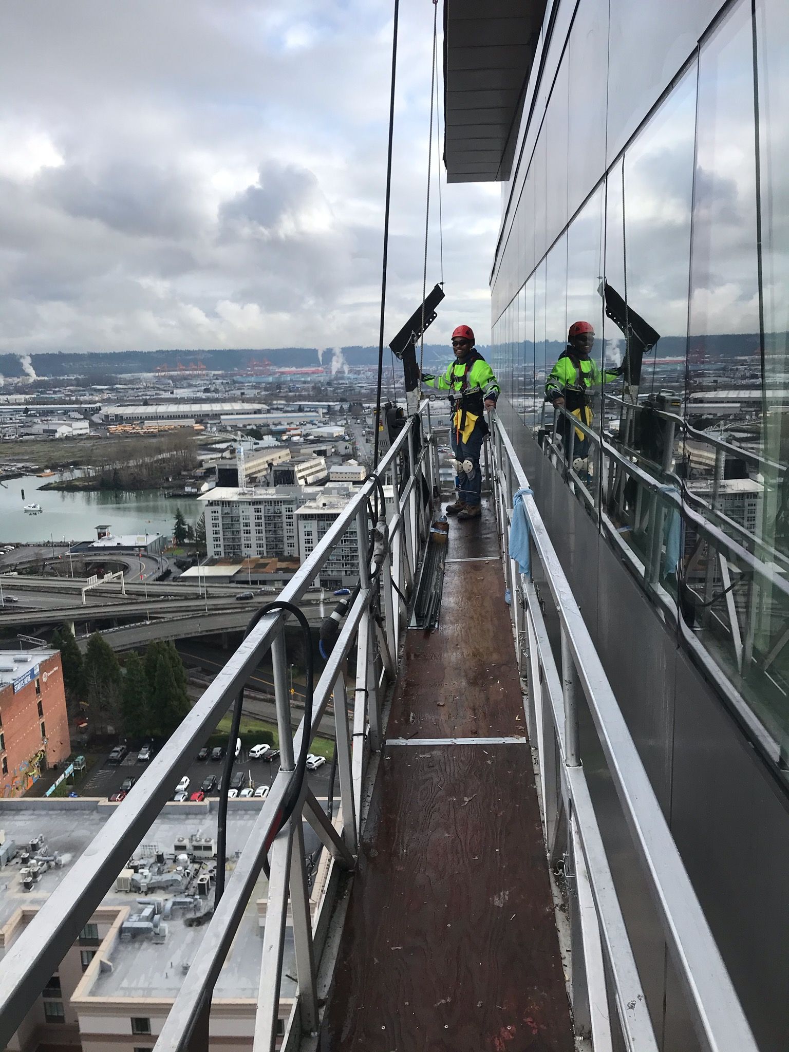 Workers in high-visibility gear on a narrow rooftop walkway above a city and river, with one person signaling.