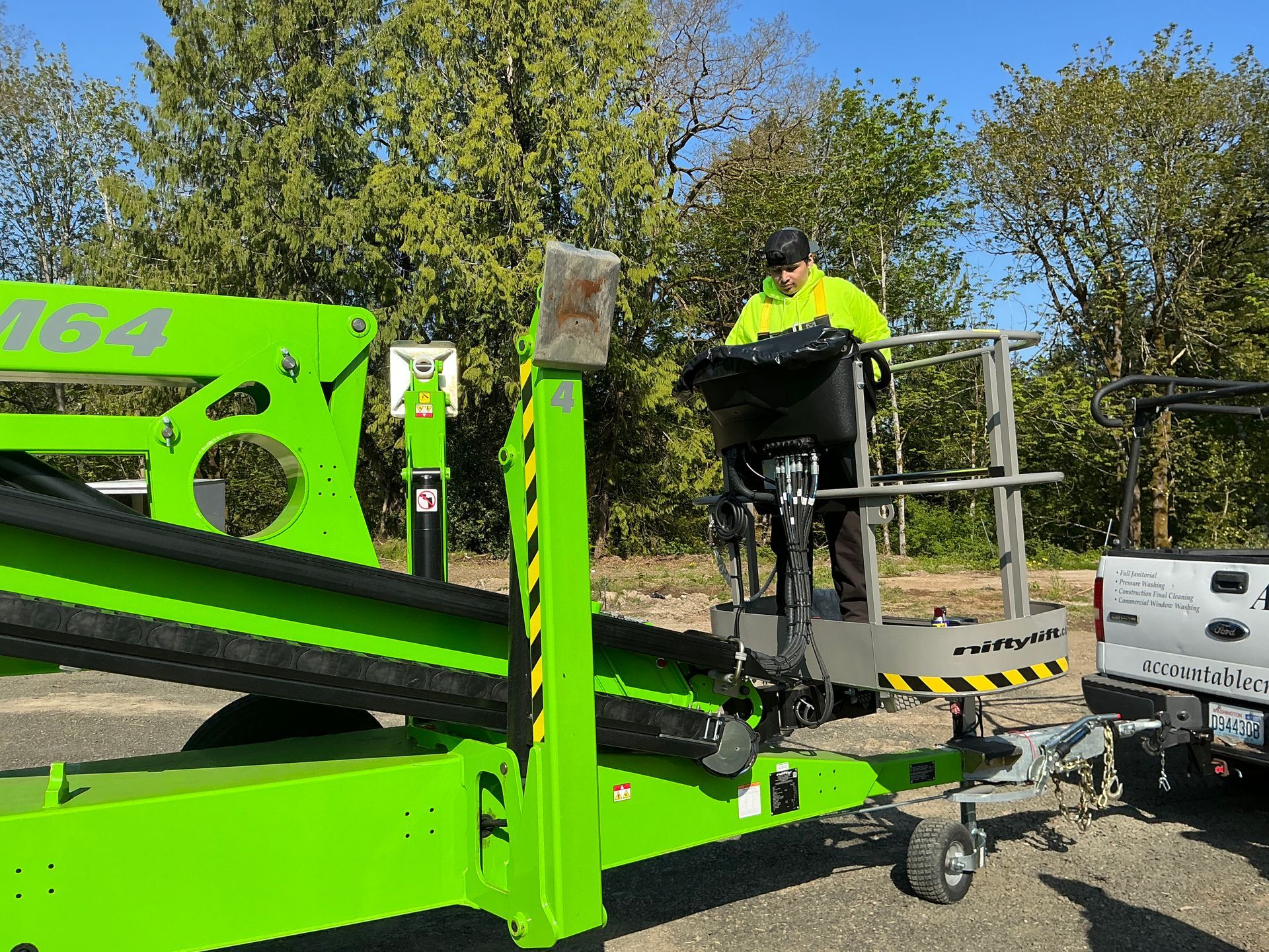 Worker in neon jacket standing on a bright green lift beside a truck outdoors