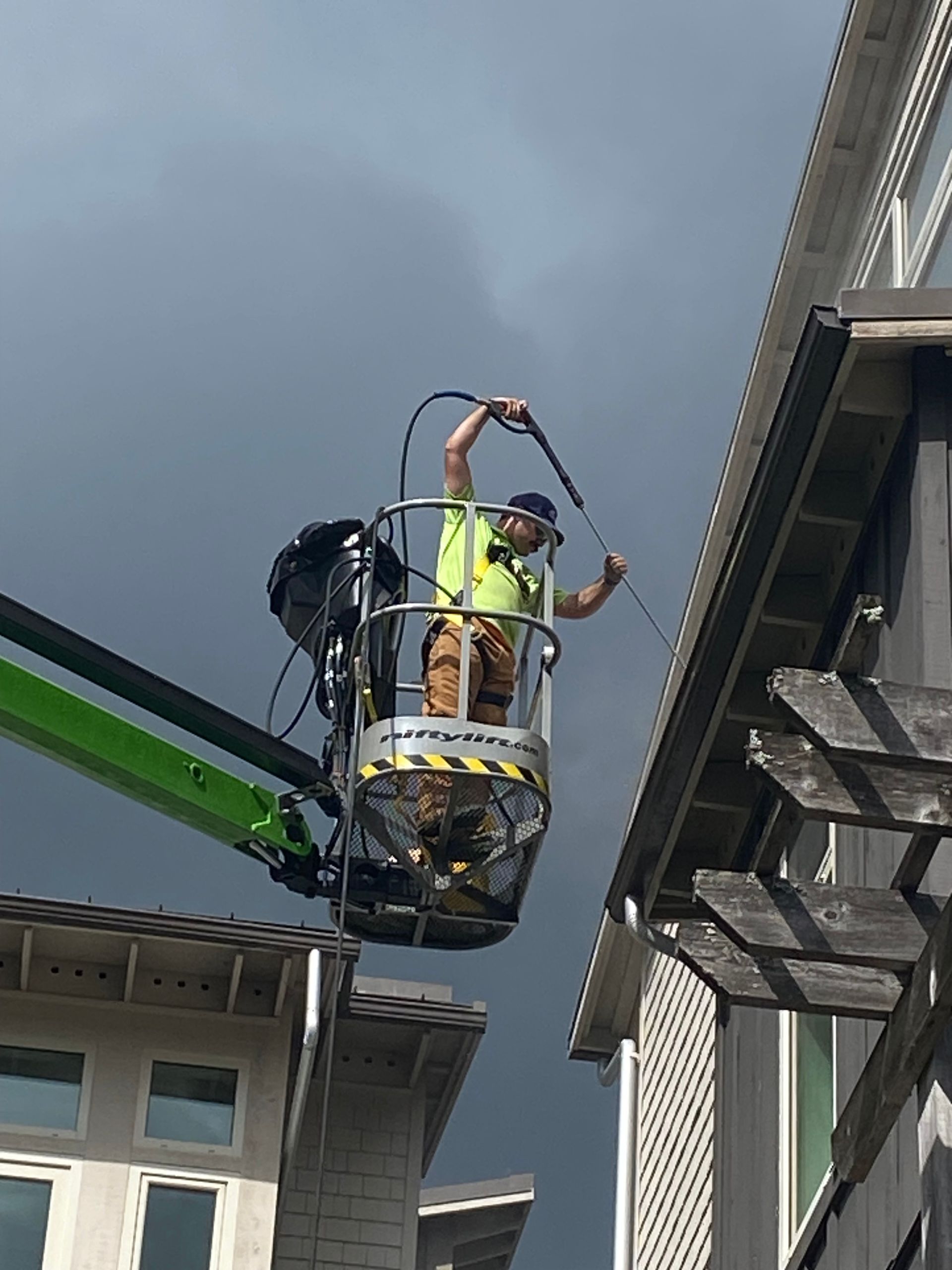 Worker in a lift painting or repairing a building exterior under a cloudy sky