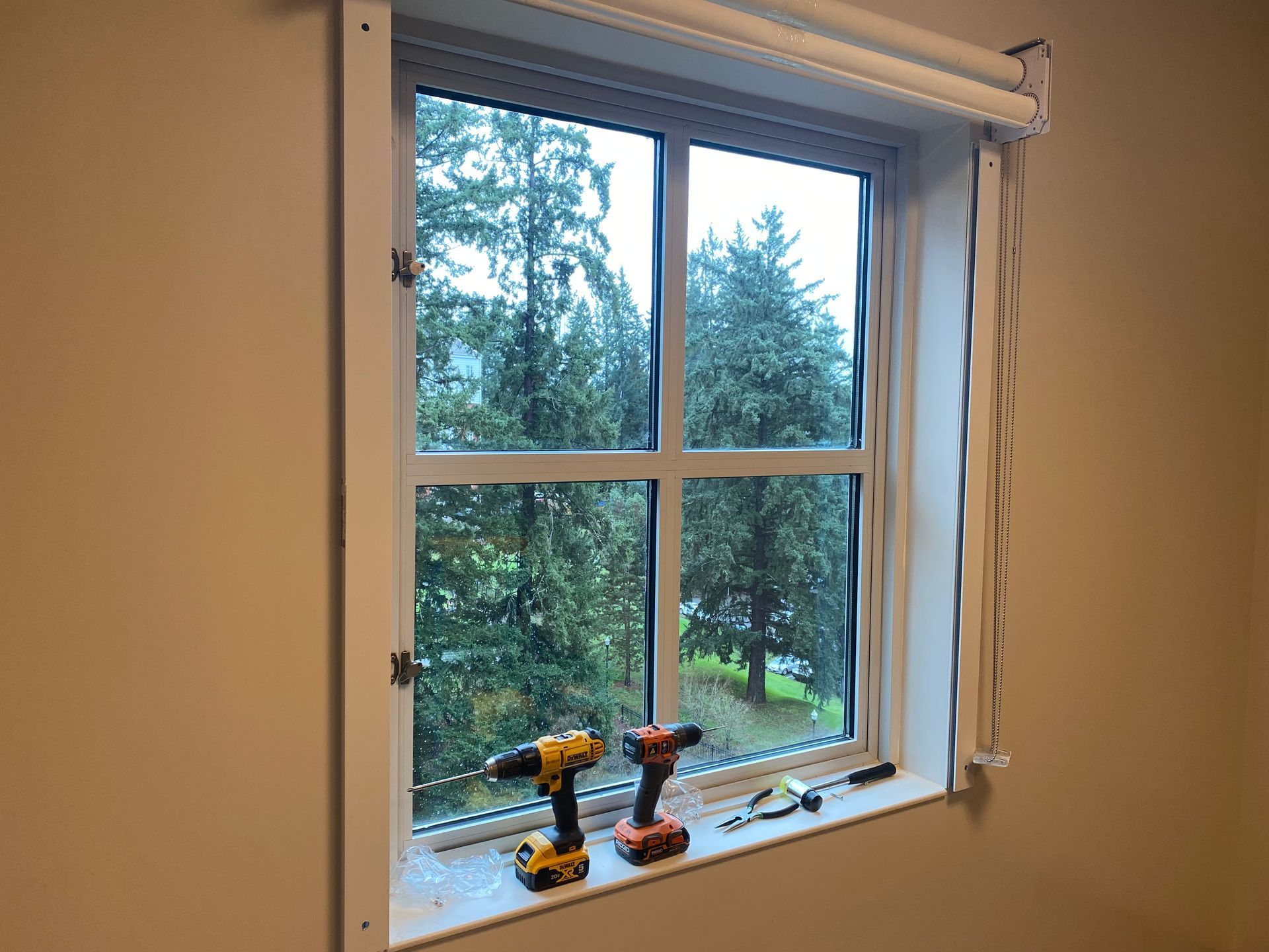 Window with a white frame, open view of trees, and two cordless drills on the sill