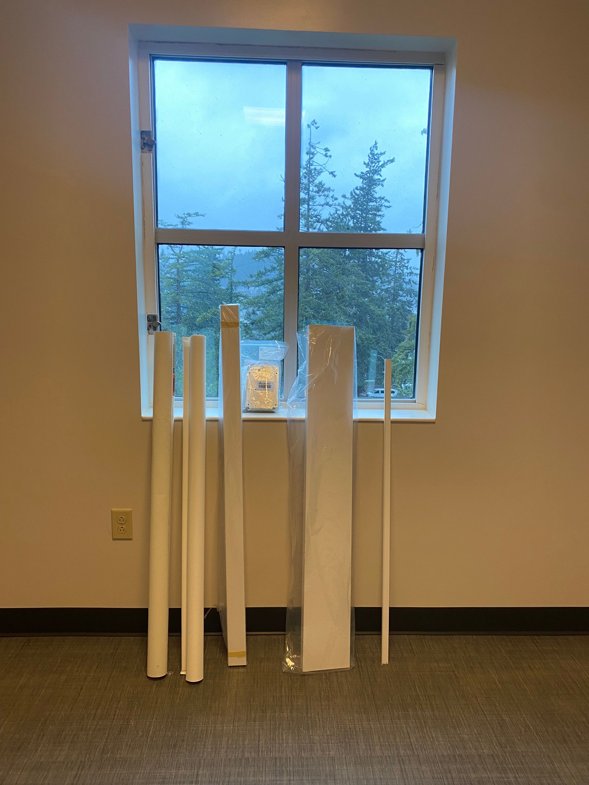 Several white rolled materials stand in front of a window in a plain room.