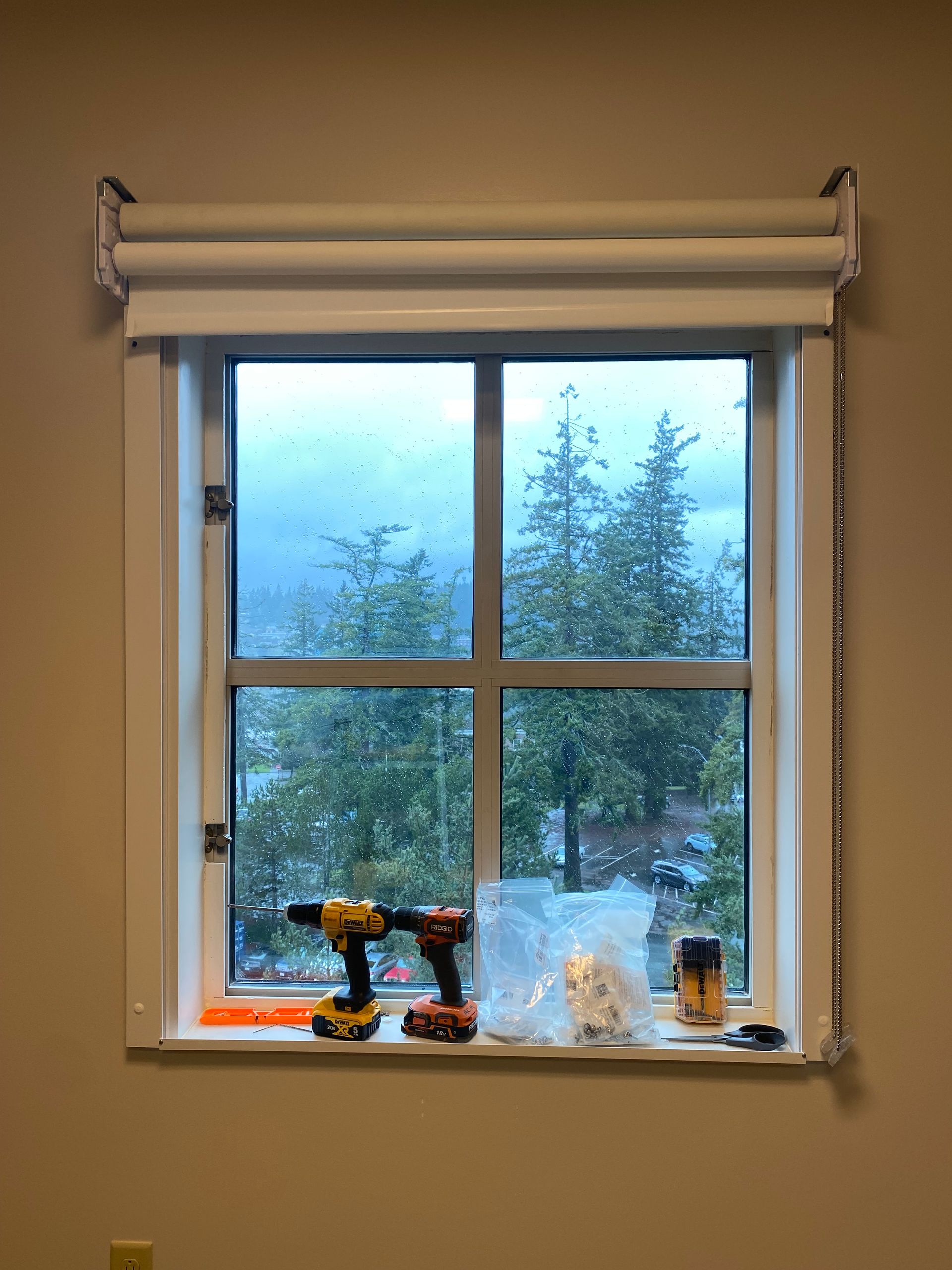 Window with blue curtains, rainy view outside, and tools plus small items on the sill inside.
