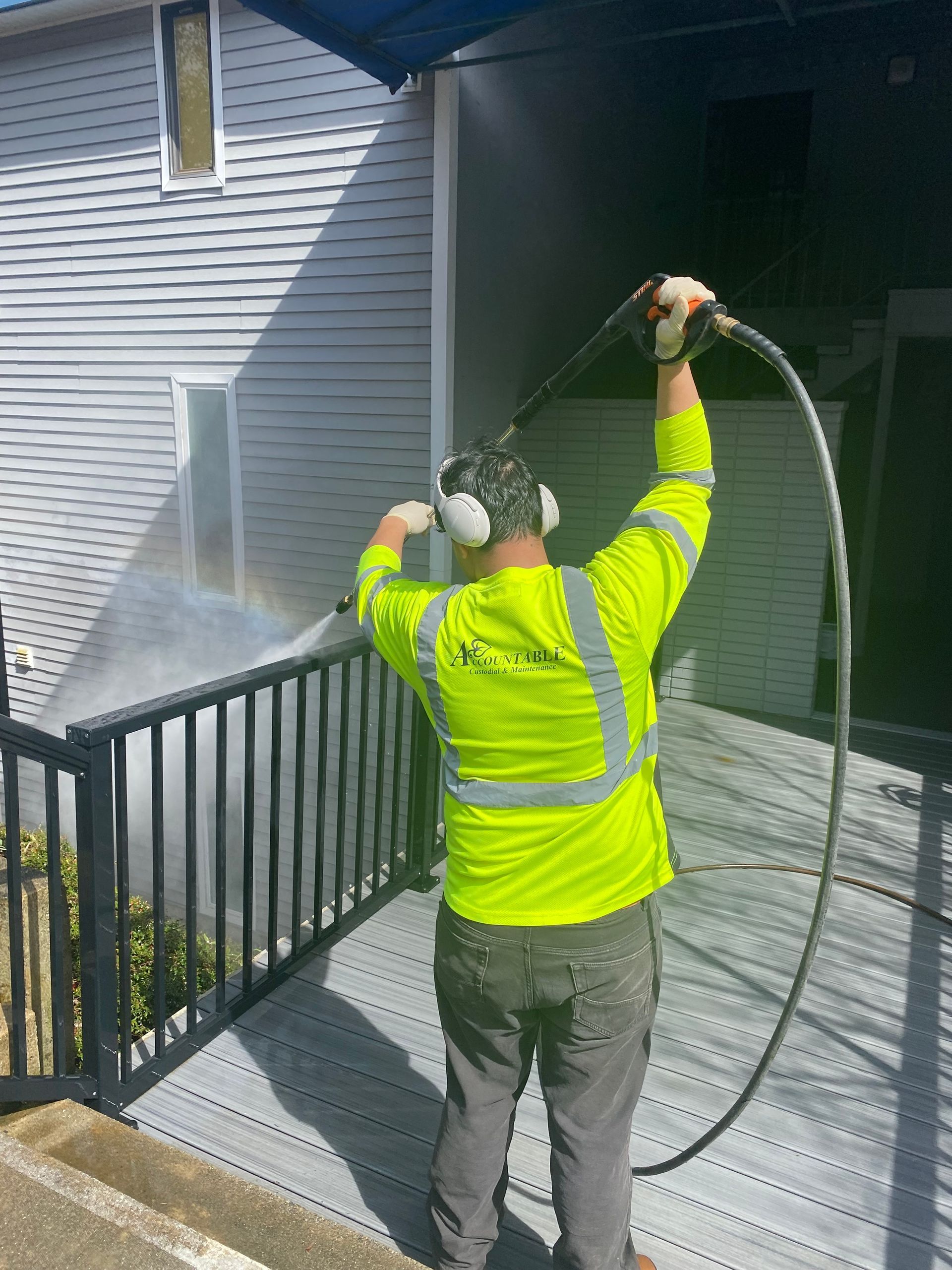Worker in neon safety jacket power washing a concrete stairway beside a building.