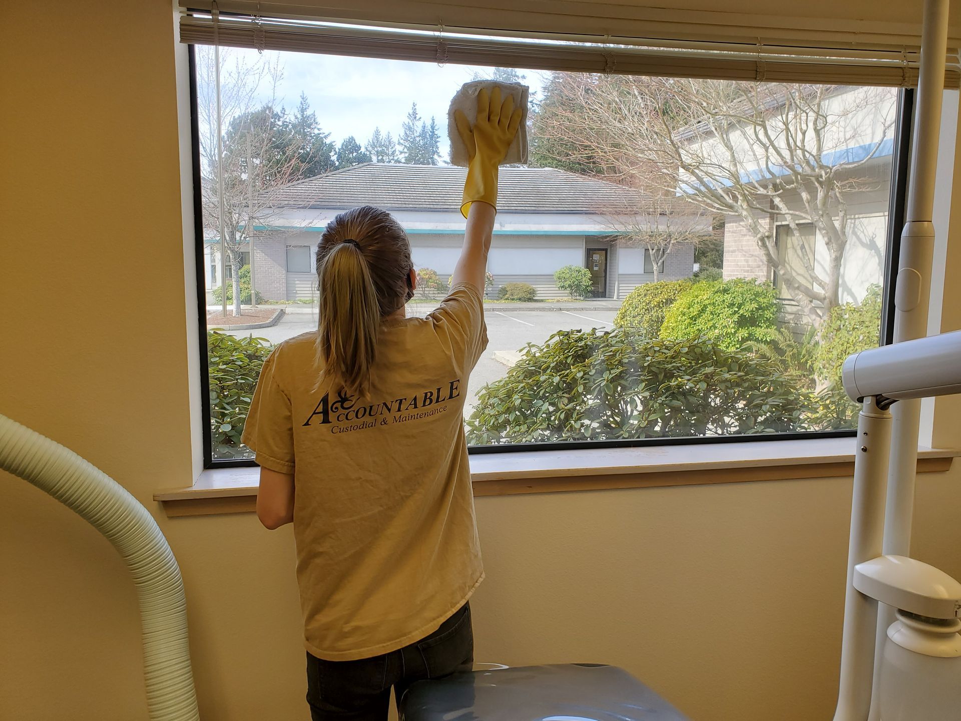 Person cleaning a window with a yellow duster, looking out at a suburban street.