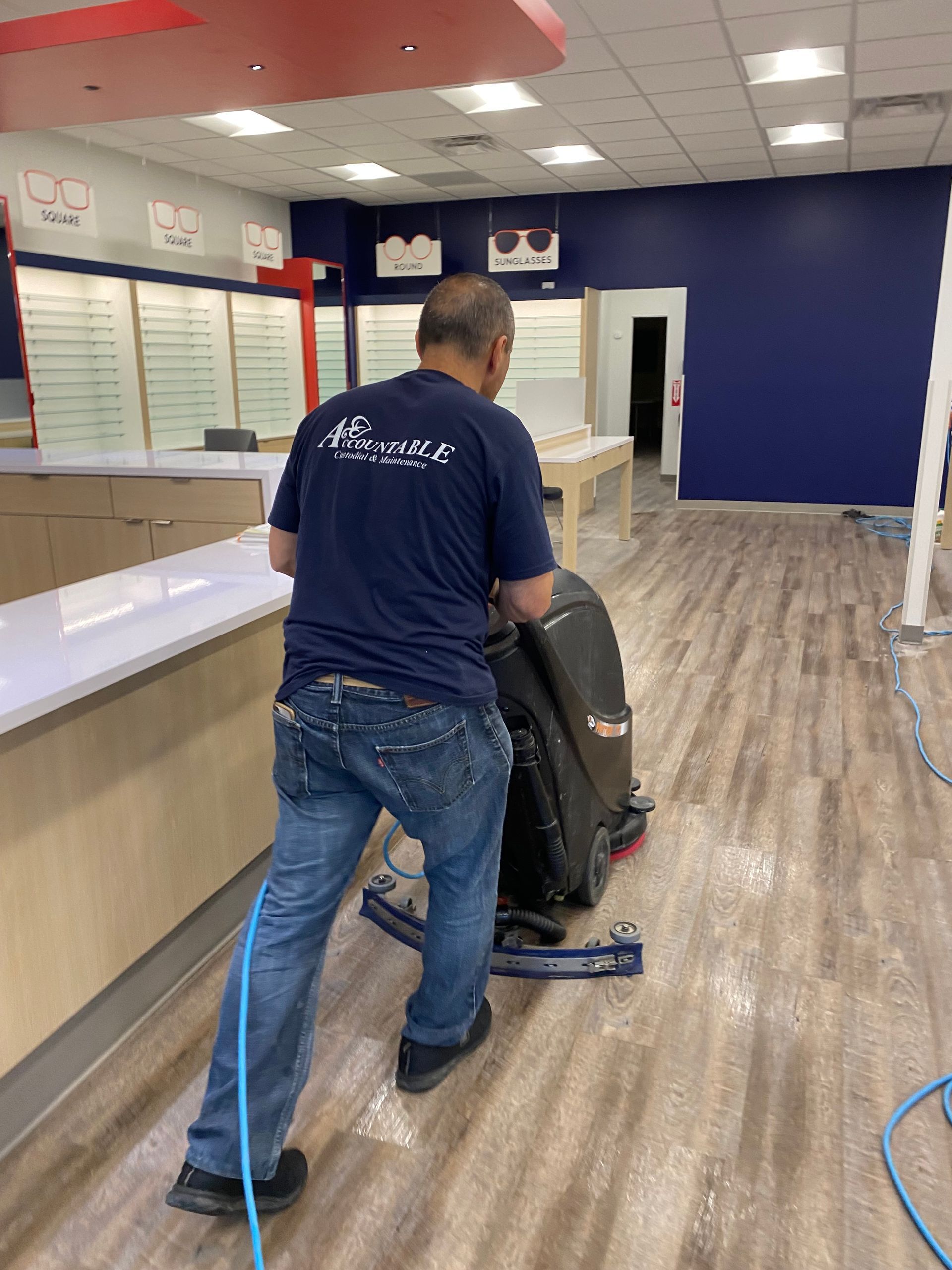 Person pushing a carpet cleaning machine across a lobby with blue walls and wood-look flooring