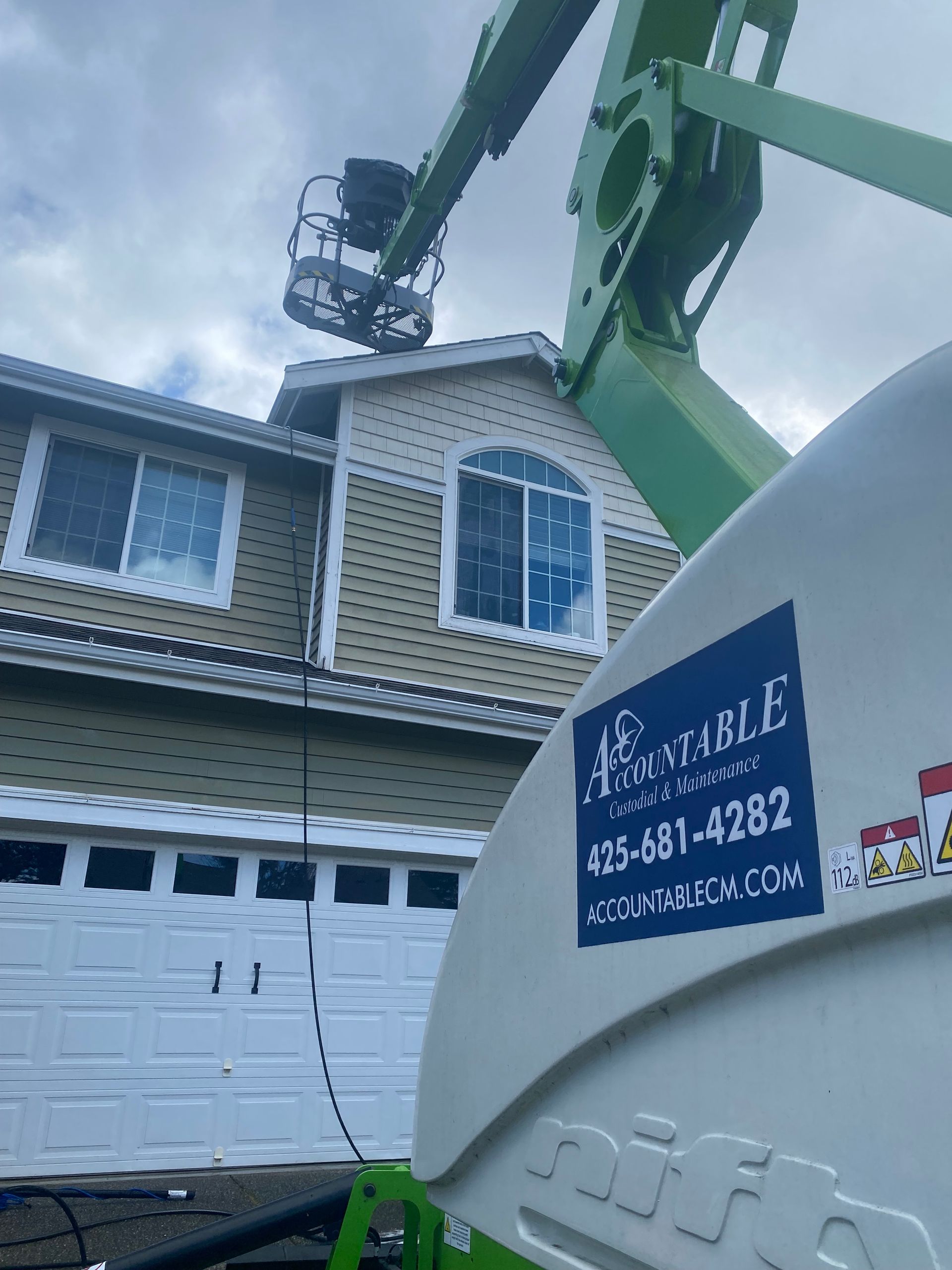 White house with garage and a crane lifting roof materials beside a green boom truck