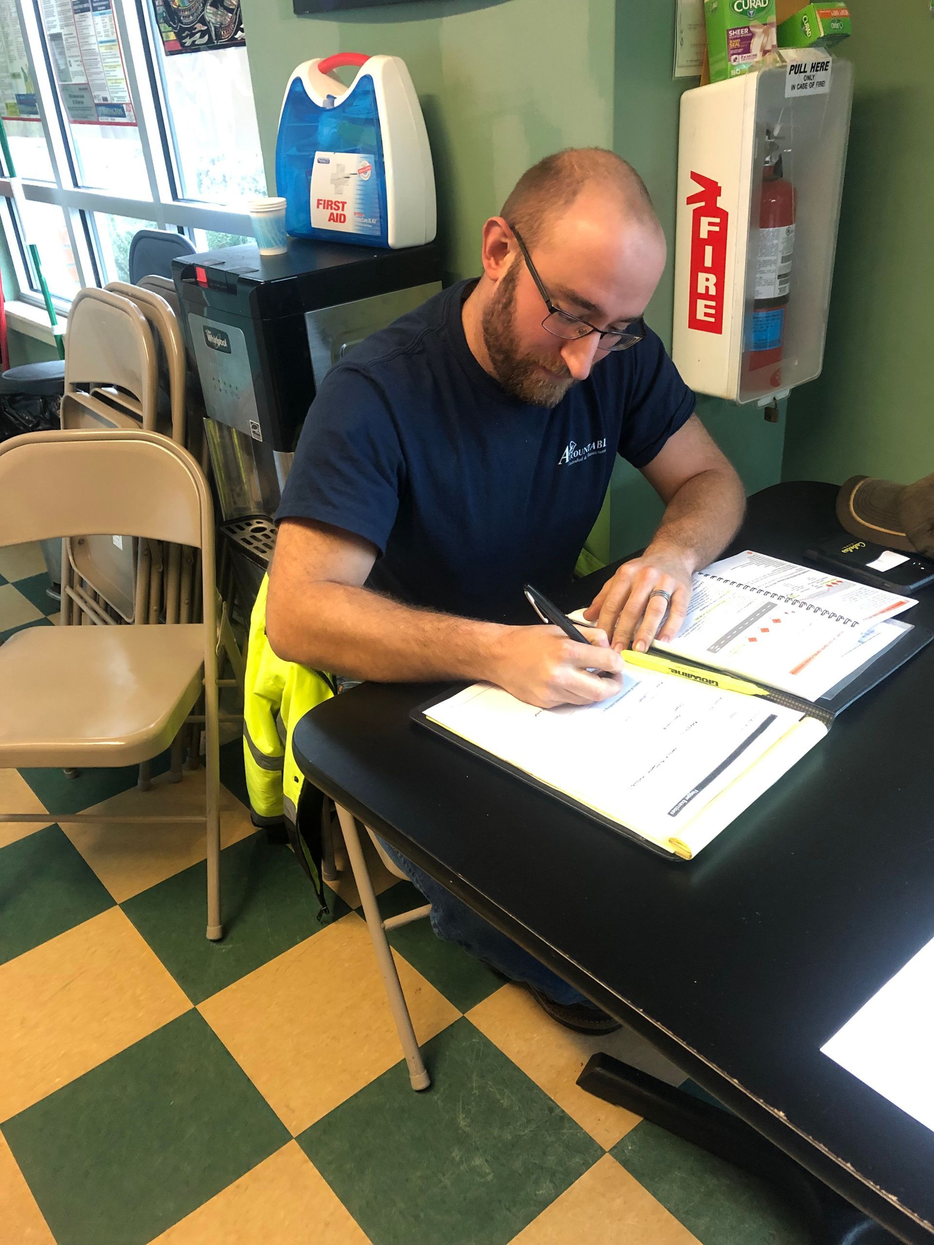 Man signing papers at a table in a tiled room near a doorway and chairs