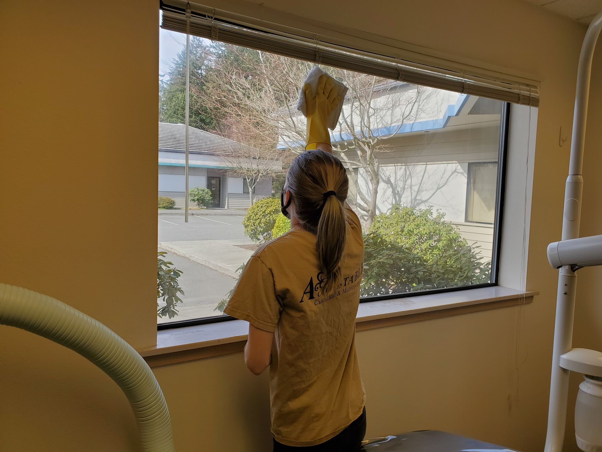 Person standing at a window, reaching up toward the blinds in a room with exercise equipment.