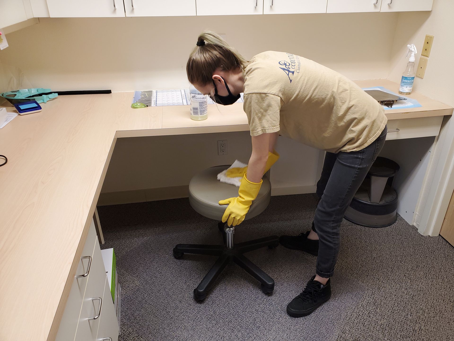 Person wearing yellow gloves adjusts a black office chair in a cluttered workspace.