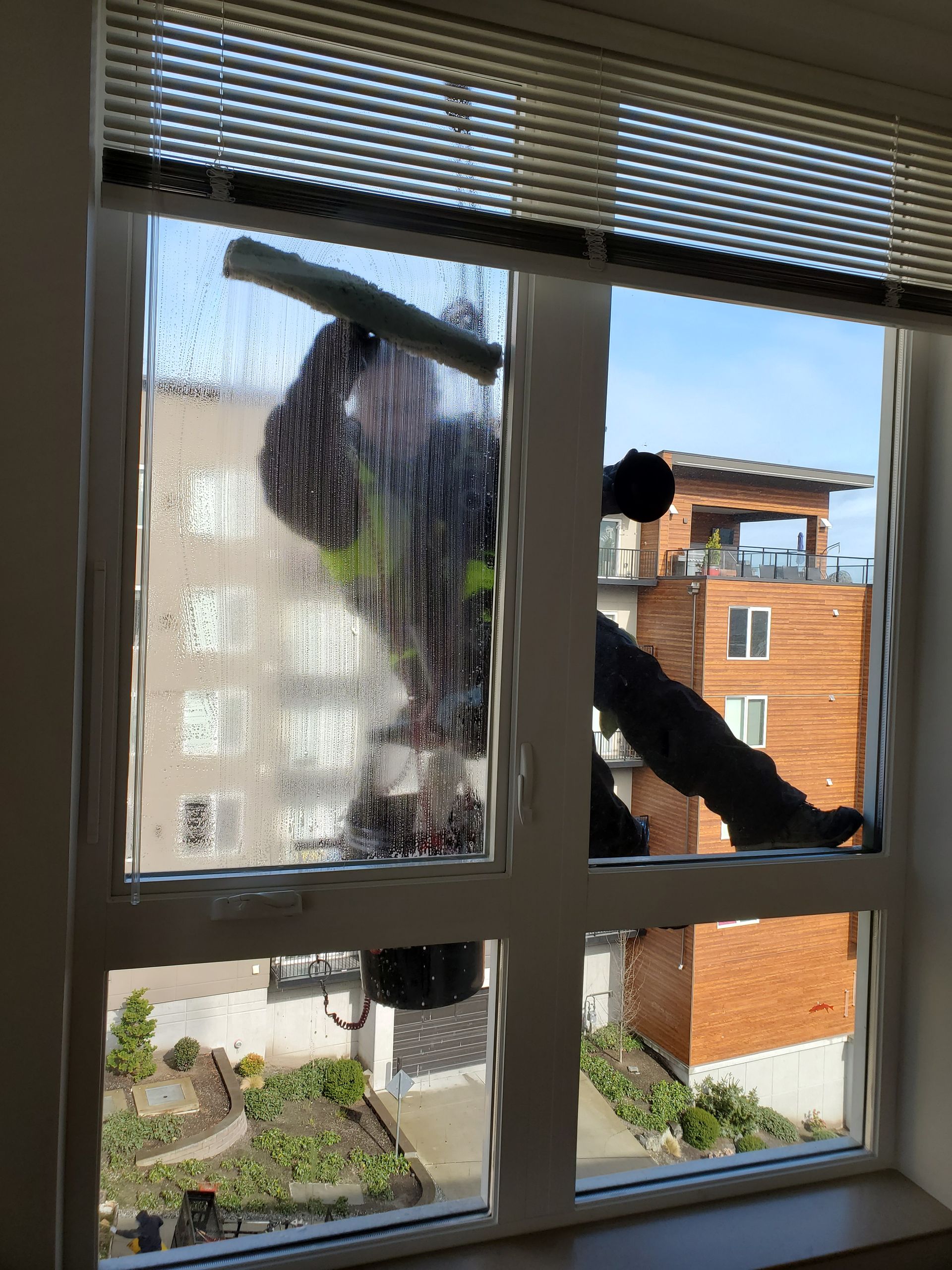 Person outside a window washing the glass with a long-handled tool, city buildings visible beyond.