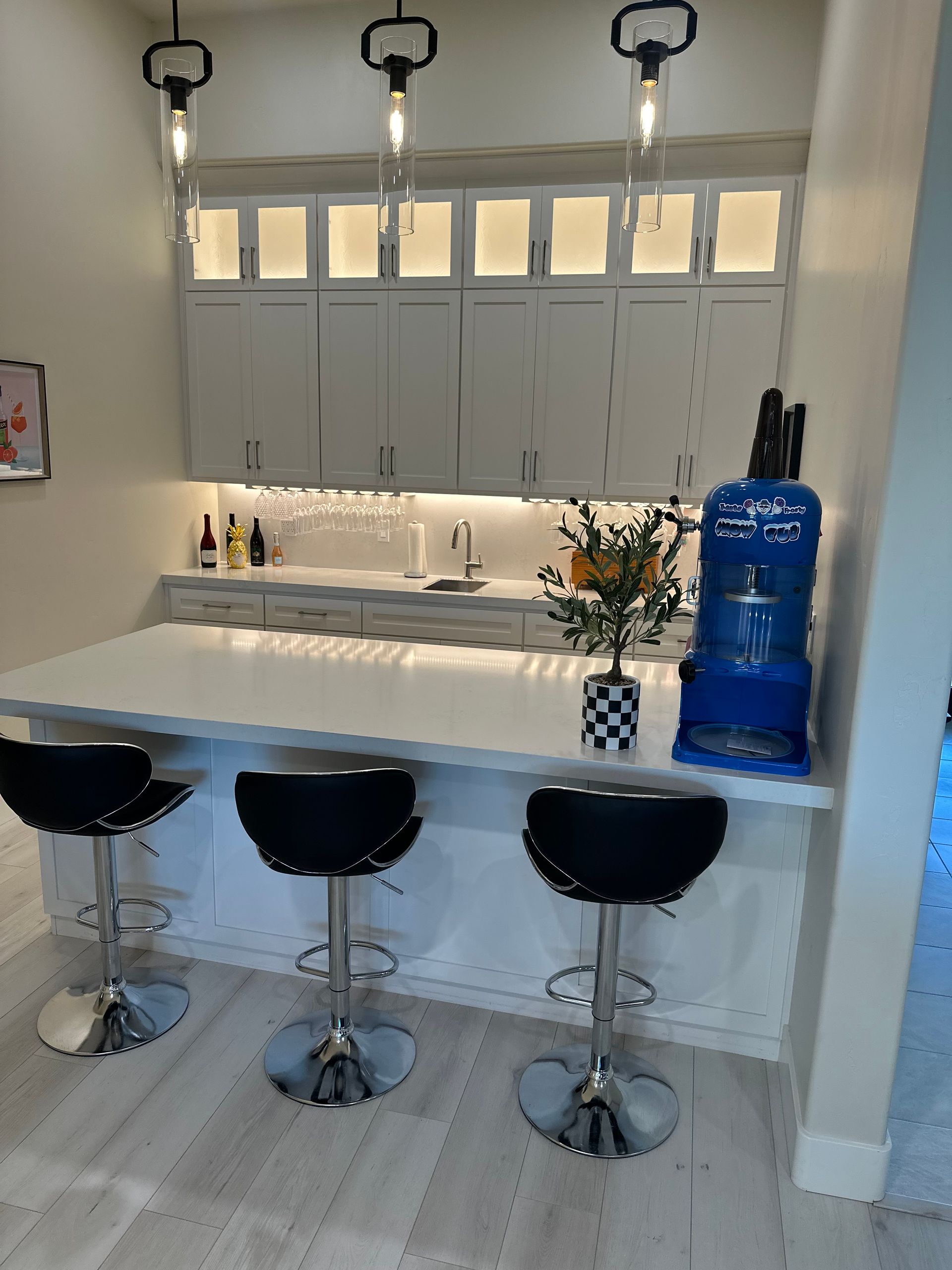 A kitchen with white cabinets and black stools and a blue water dispenser