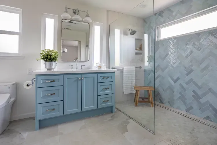 A bathroom with blue cabinets and a walk in shower.