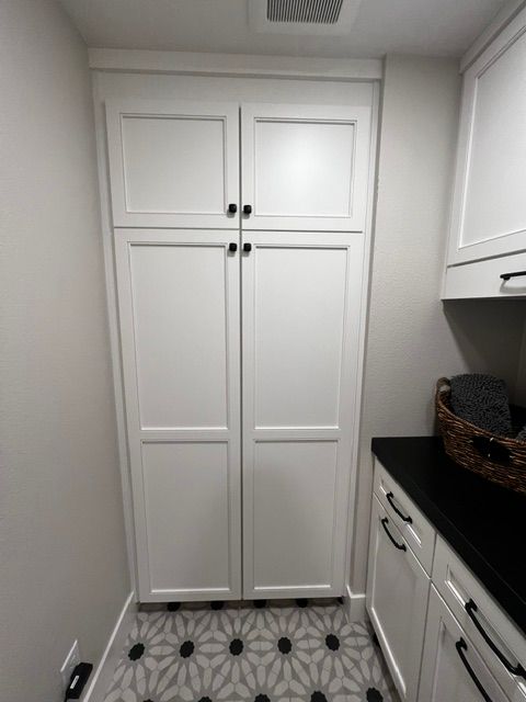 A laundry room with white cabinets and black counter tops.