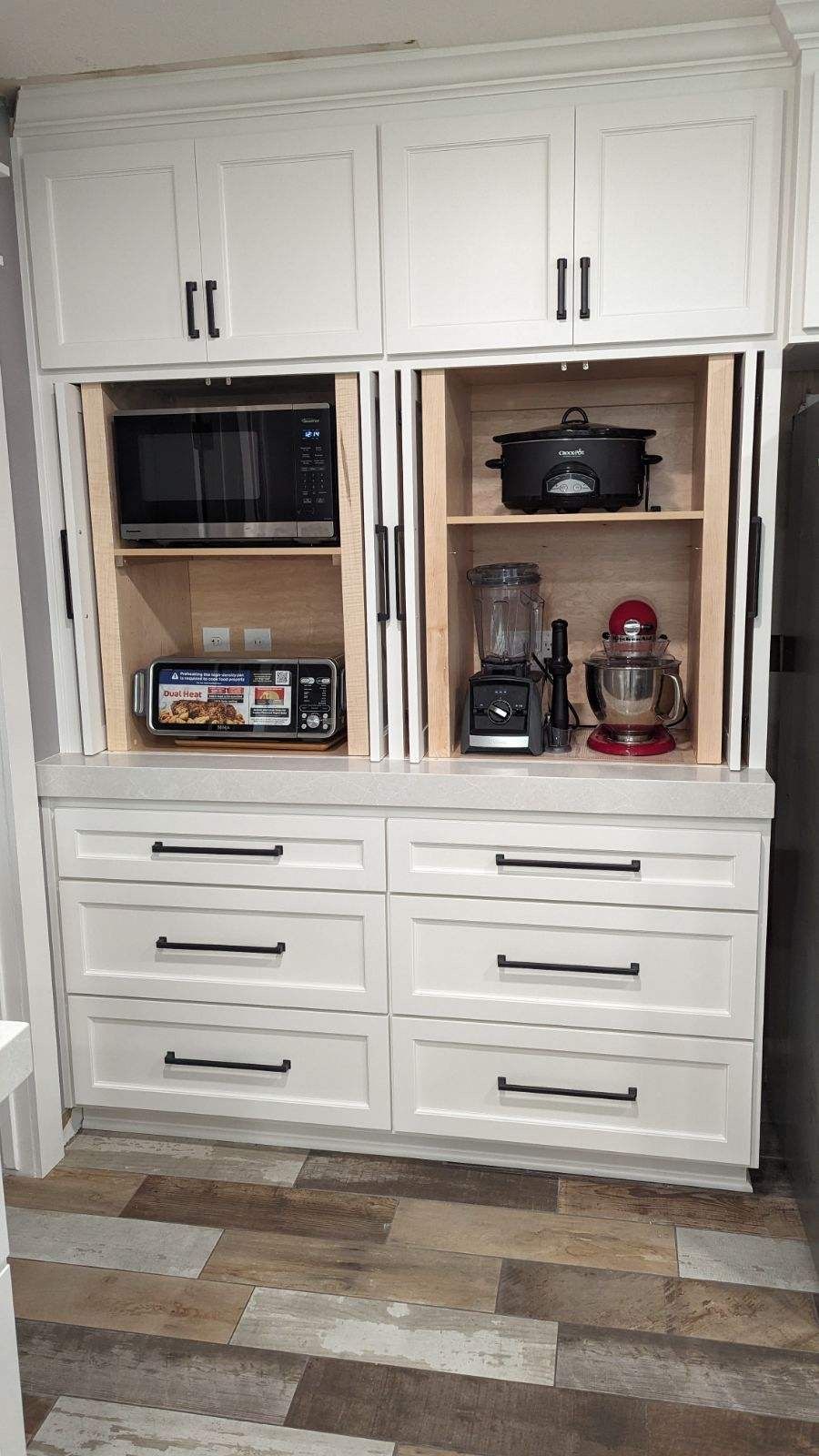 A kitchen with white cabinets , drawers , a microwave and a blender.