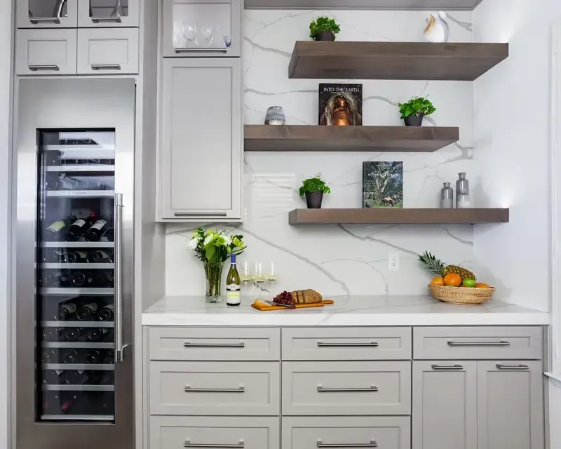 A kitchen with white cabinets , stainless steel appliances , a wine cooler and shelves.