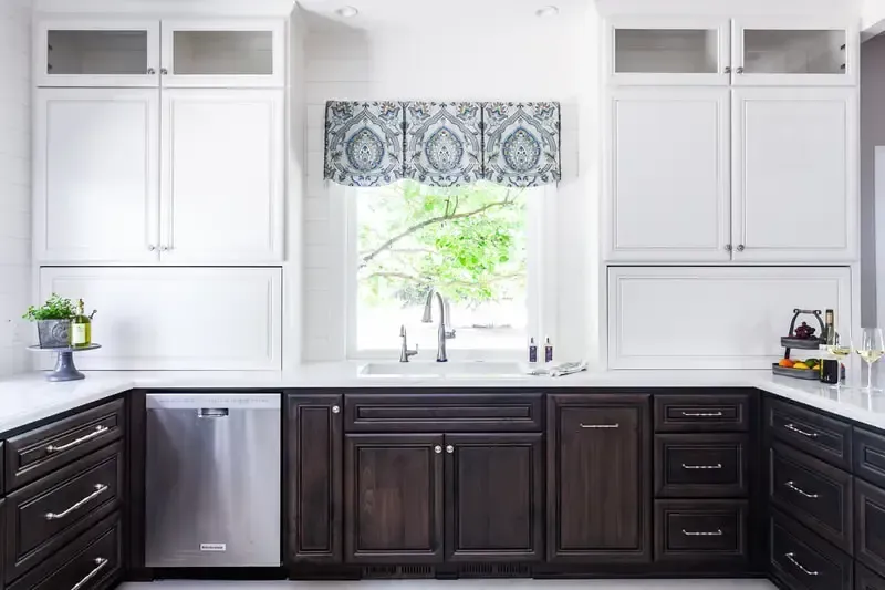 A kitchen with white cabinets , dark cabinets , stainless steel appliances , a sink , and a window.