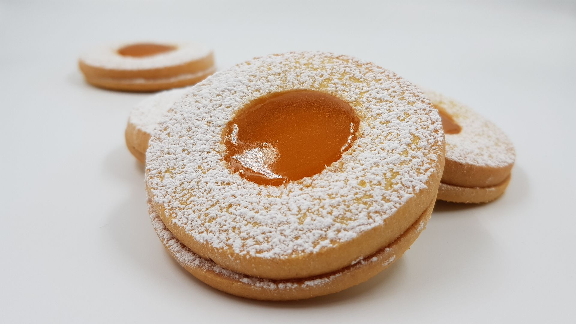 Primo piano di tre biscotti Linzer spolverati con zucchero a velo su una superficie bianca.