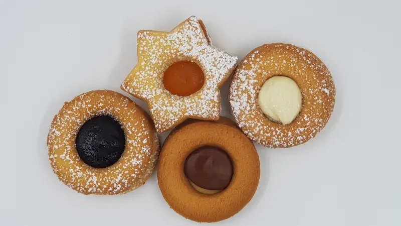 Quattro tipi diversi di biscotti sono disposti uno sopra l'altro su una superficie bianca.