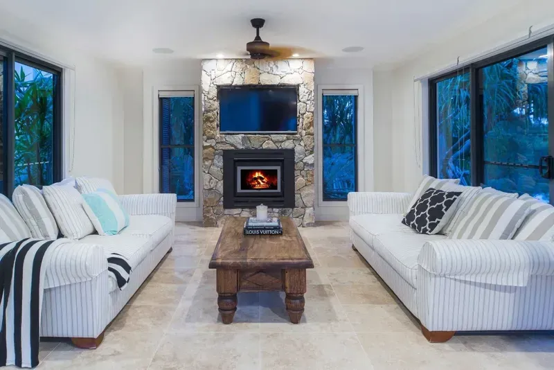 Living Room With Two White Striped Sofas Facing a Fireplace With a Lit Fire and a Mounted Tv — North Coast Tiles in Grafton, NSW 