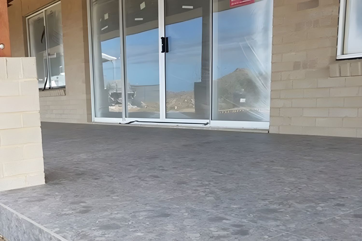 A Building's Entrance With a Gray Concrete Patio and Sliding Glass Doors, Reflecting a Bright Outdoor Scene — North Coast Tiles in Grafton, NSW